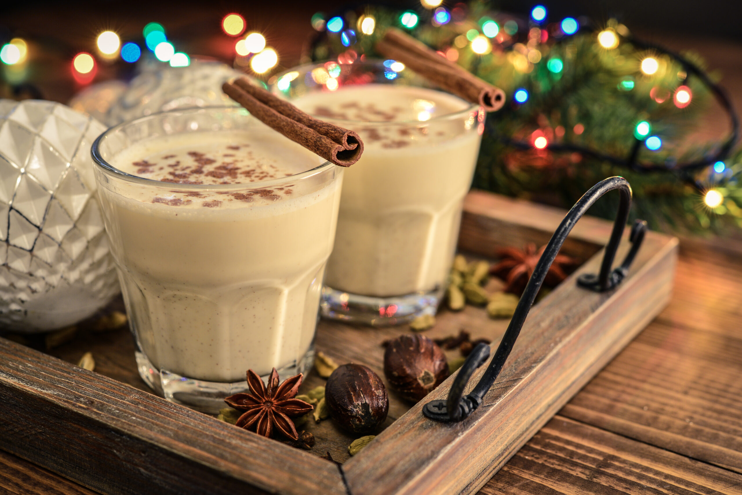 Traditional christmas drink eggnog in glass with spices and  christmas lights on wooden background