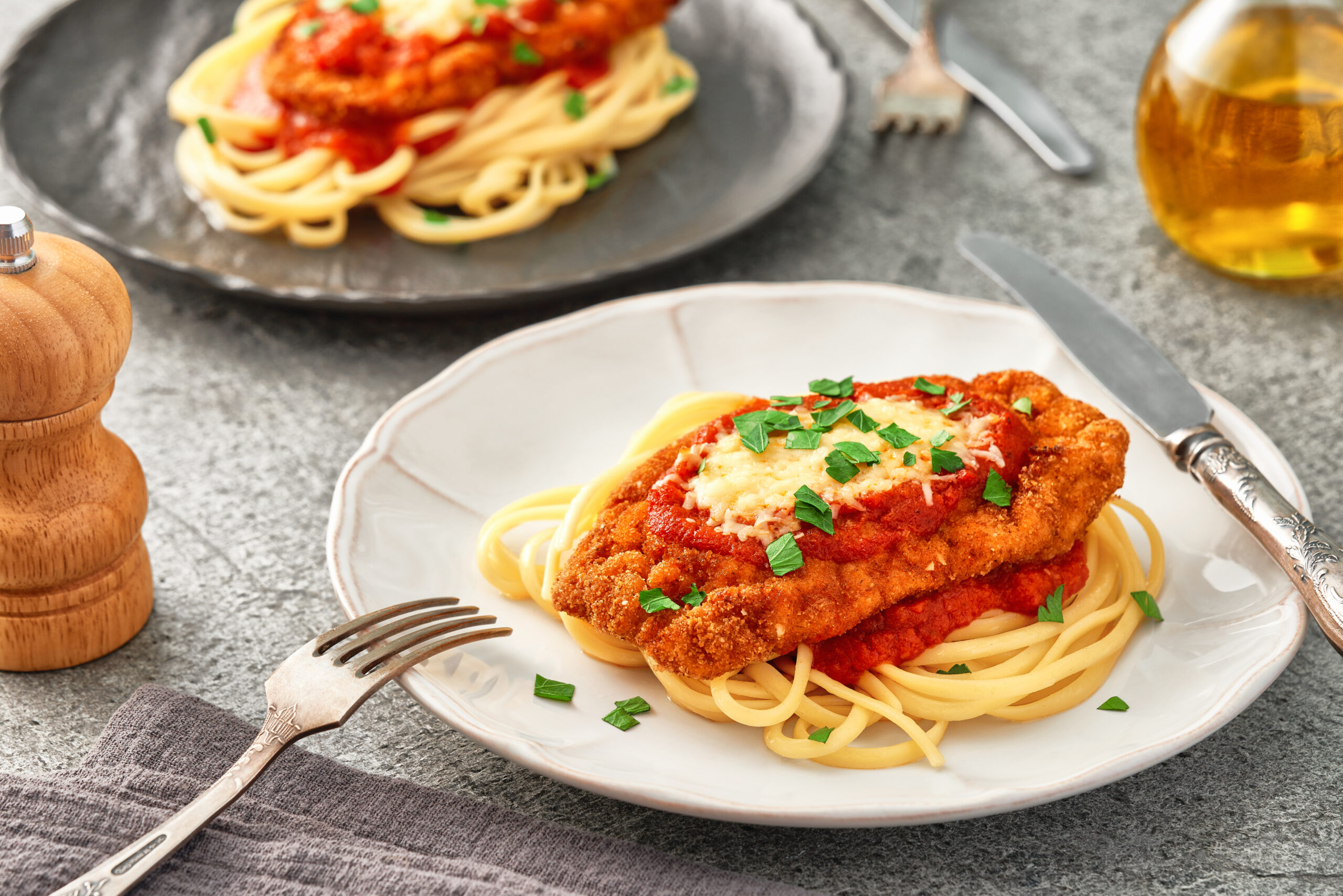 Plates of Chicken Parmesan with spaghetti on a gray stone background. Studio shot.