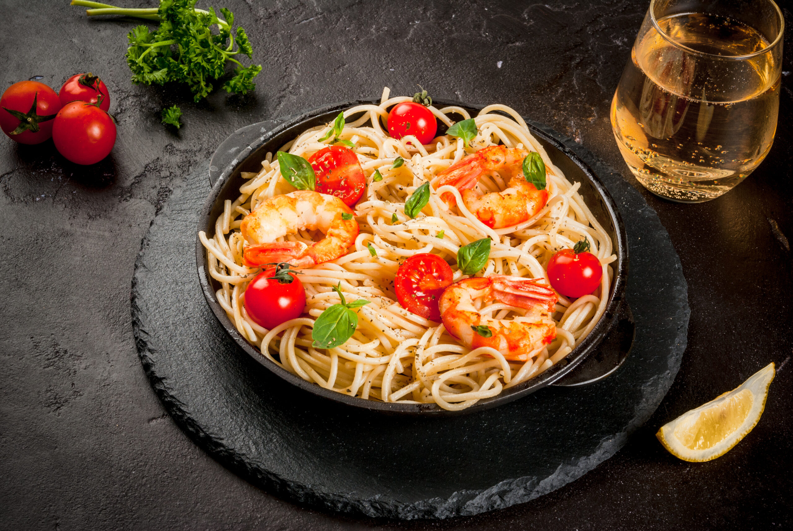 Seafood. Shellfish. Pasta with grilled prawns shrimps, with tomatoes, fresh herbs (basil) and spices. On  cast-iron frying pan, black concrete table, with glass of white wine, Copy space